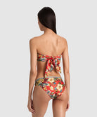 A woman shown from the back wearing a strapless floral bikini with a large bow detail at the back of the top and high-cut bottoms, against a light gray studio background.