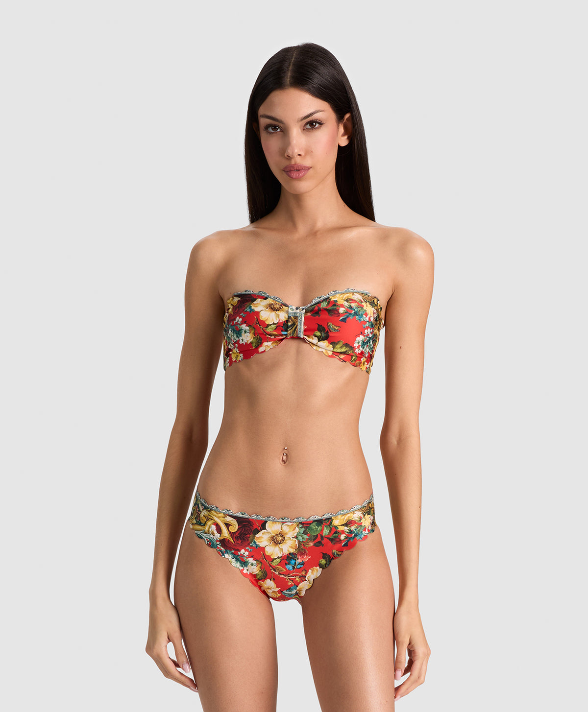 A woman modeling a strapless bikini set with a vibrant red, yellow, and green floral print against a solid light gray background.