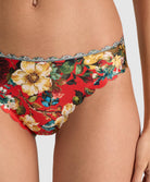 Close-up of a model wearing red floral bikini bottoms with a silver scalloped lace trim, featuring large yellow and white flowers with green leaves.