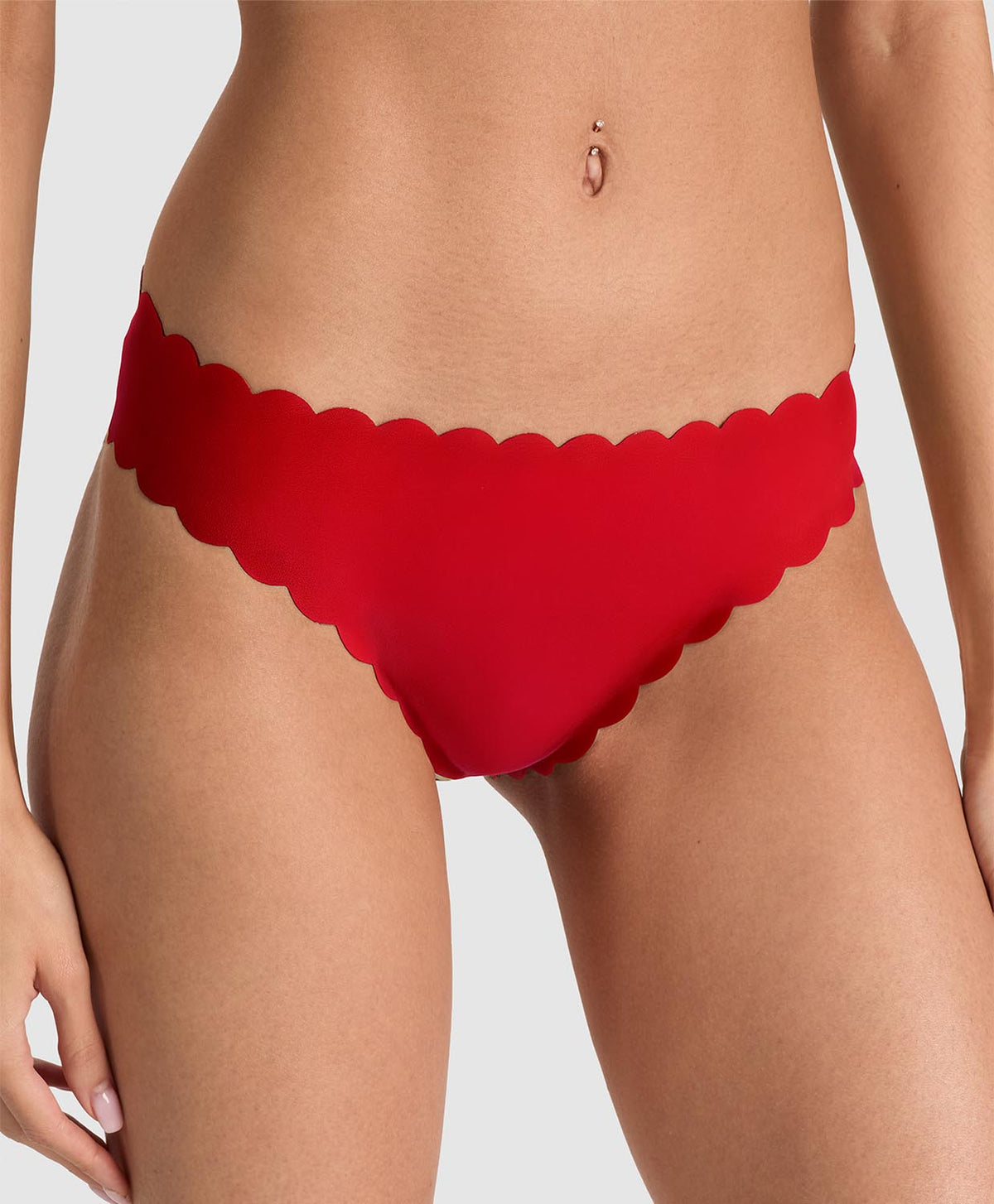 Red scalloped-edge bikini bottom worn by a model, shown from the waist to upper thighs against a light gray studio background.