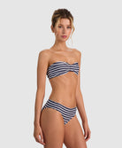 A woman modeling a two-piece bikini with navy and white horizontal stripes against a light gray studio background.