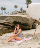 Young girl wearing a striped one piece bikini sitting on a towel on the beach.