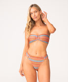 A woman wearing a striped bandeau bikini standing against a white wall. 