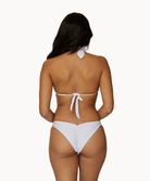 Back view of a woman wearing a white halter top bikini in front of a white background. 