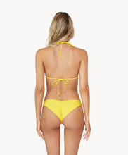 Blonde woman wearing a yellow ruched triangle top bikini facing backwards towards a white wall.