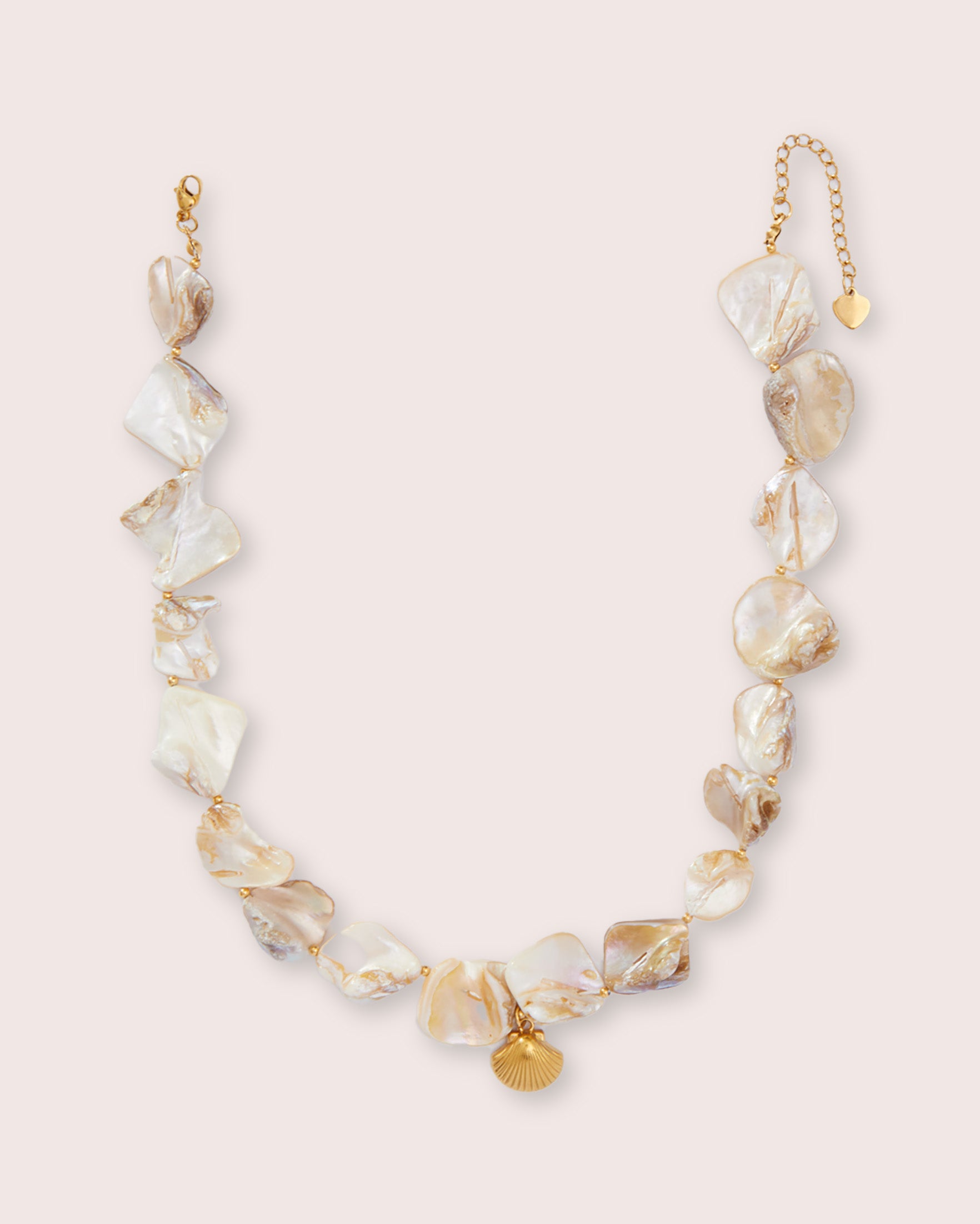 A necklace with small stones and gold shell piece against a white wall.