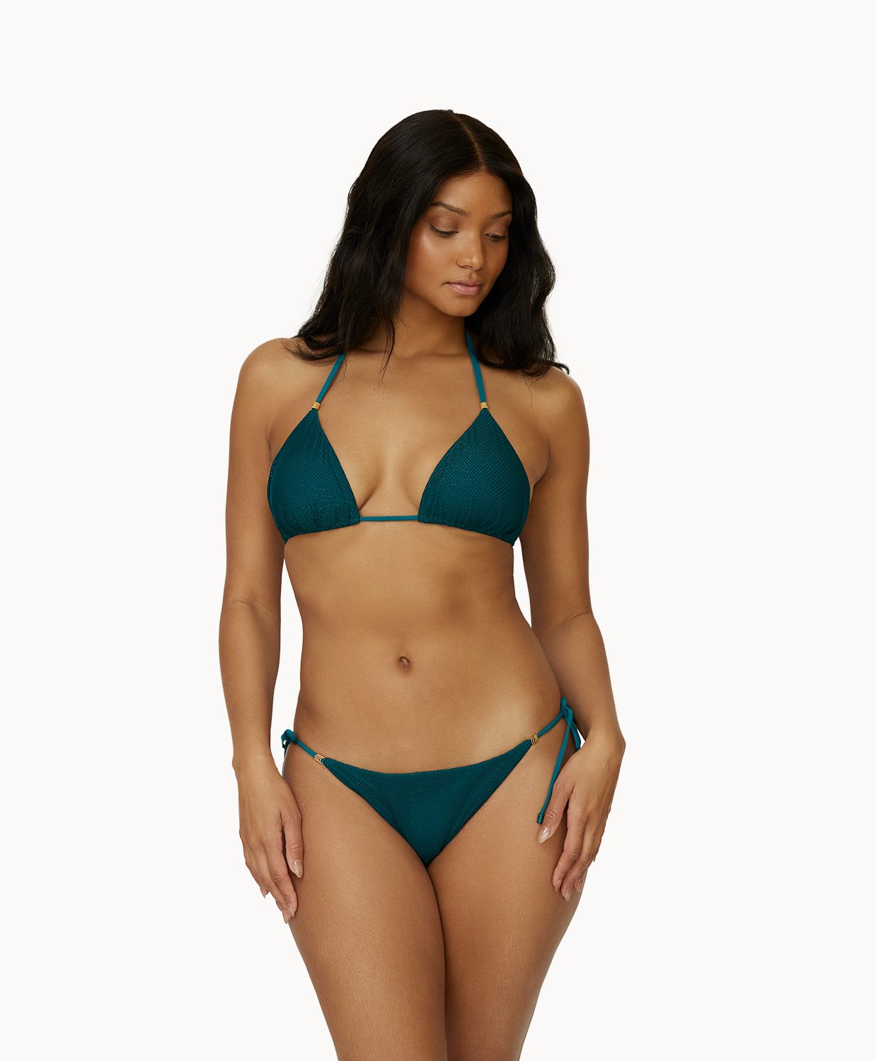 A woman wearing a green triangle top bikini standing against a white wall.