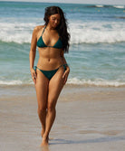 A woman wearing a green triangle top bikini walking on the beach near the ocean. 