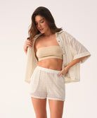 Woman wearing a beige bandeau top and white lace shorts with a matching jacket on a light background