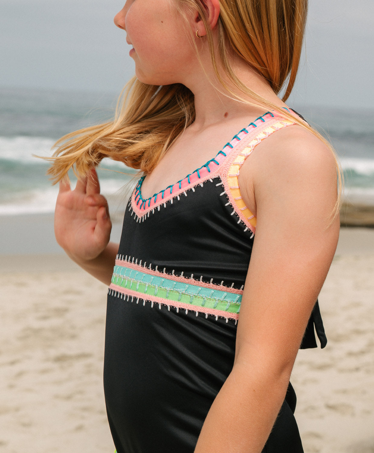 Young girl wearing a black swimsuit with colorful top design on a beach