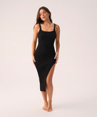 Woman wearing a black ribbed dress with a slit on a white background