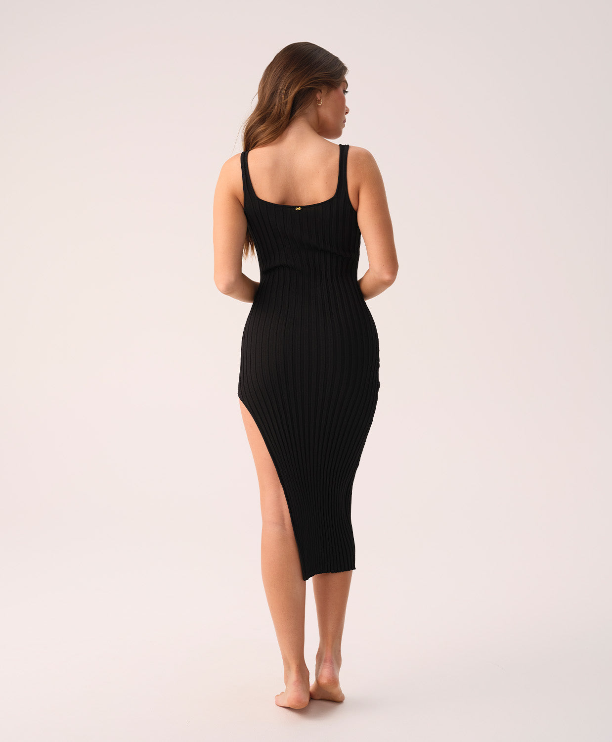 Woman wearing a black ribbed dress with a slit on a white background