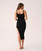 Woman wearing a black ribbed dress with a slit on a white background
