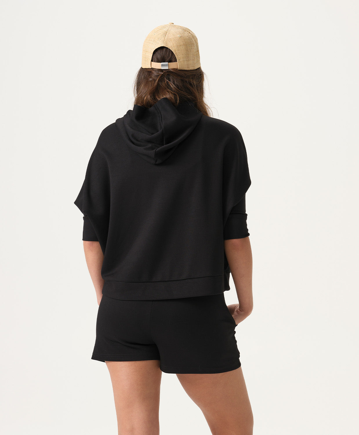 Woman wearing a black hoodie and shorts with a beige cap on a white background