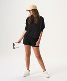Woman wearing a black outfit with a beige cap and white sneakers on a white background