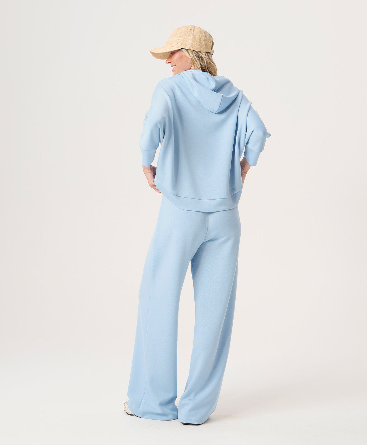 Woman wearing a light blue hoodie and pants with a beige cap on a white background