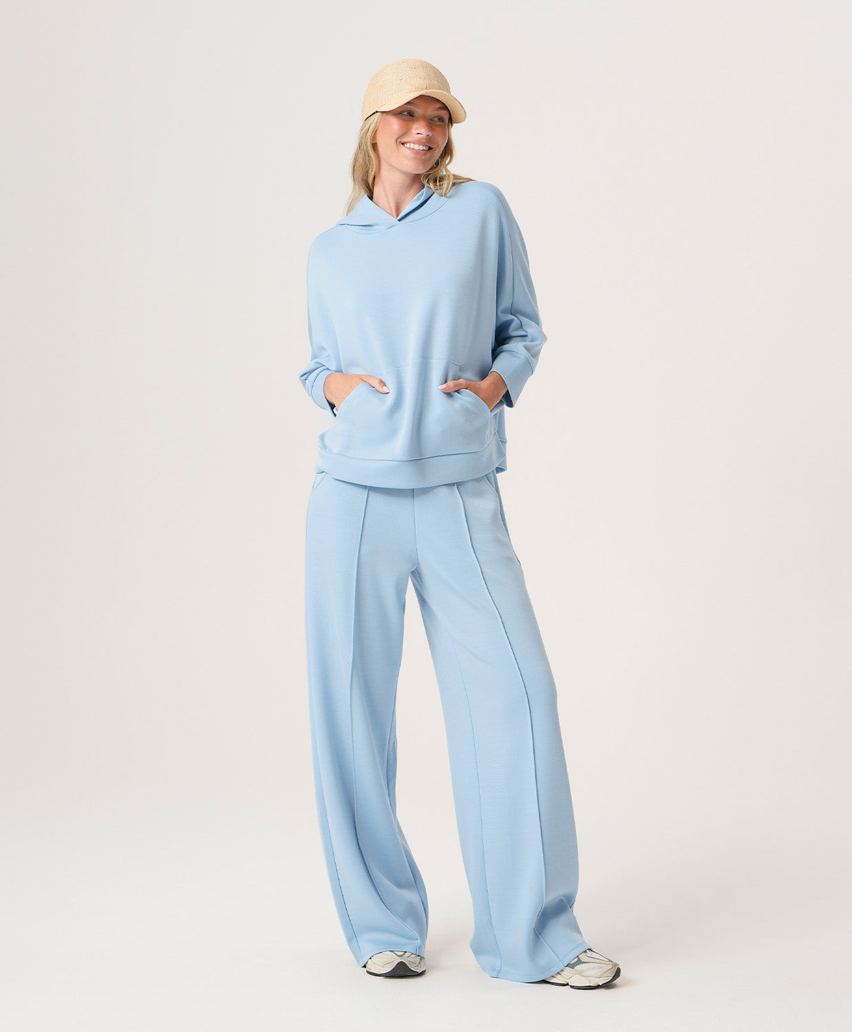 Woman wearing a light blue outfit with a beige cap on a white background