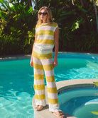 Woman in a yellow and white striped outfit standing by a pool with greenery in the background