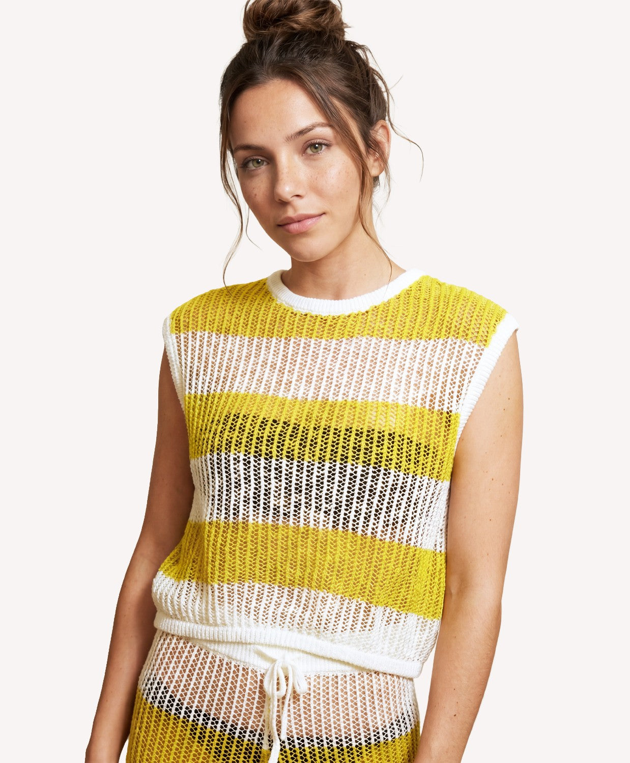 Woman wearing a yellow and white striped sleeveless top on a plain background
