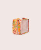 A packing cube with an orange floral print against a white wall. 