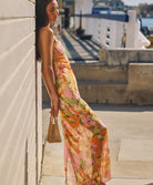 A woman wearing a long, colorful, strapless dress leaning against a brick wall.