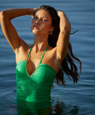 A brunette woman wearing a green one piece swimsuit standing in a pool. 