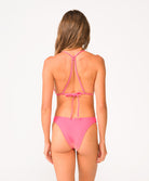 A woman wearing a pink bikini set facing away in front of a white background.