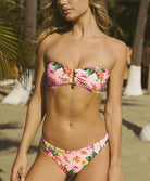 Woman wearing a pink floral bikini set on a beach with palm trees in the background