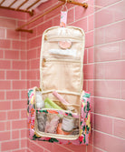 Floral-patterned toiletry bag with travel essentials against a pink tiled wall.