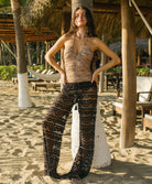 Woman in a leopard one piece standing on a sandy beach with palm trees and lounge chairs in the background.
