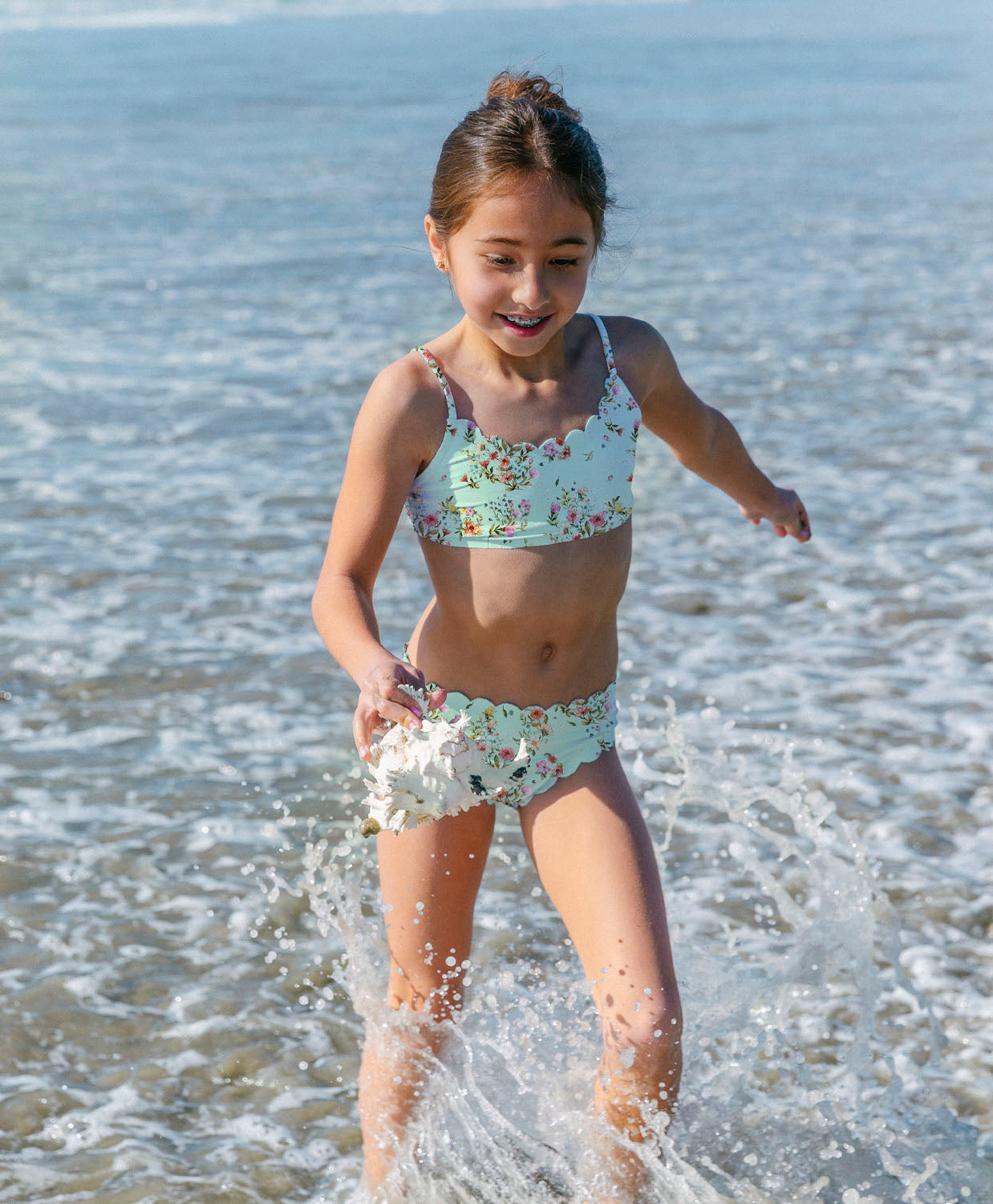 Young girl in a floral swimsuit playing in the ocean.