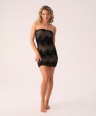 Woman wearing a black strapless dress with floral lace details on a white background