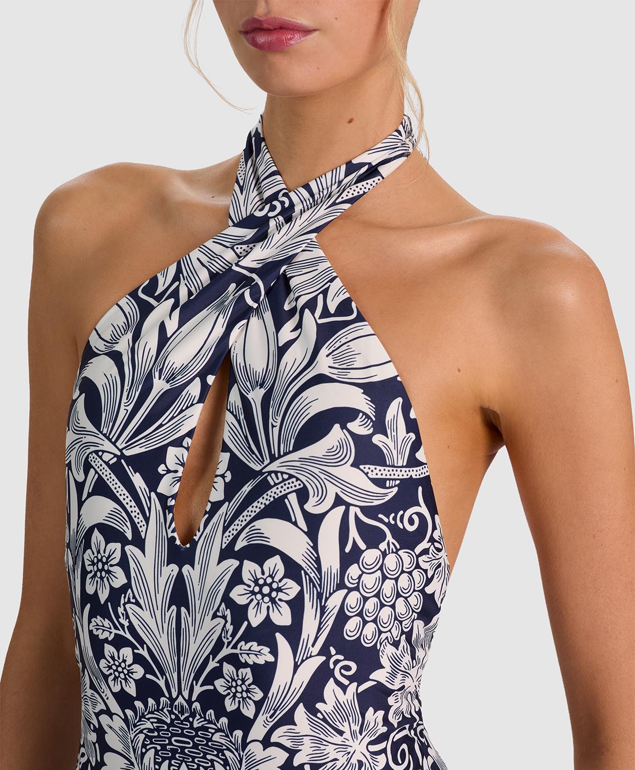 Close-up of a model wearing a halter-neck swimsuit with a navy blue and white botanical floral print, featuring a keyhole cutout at the chest.