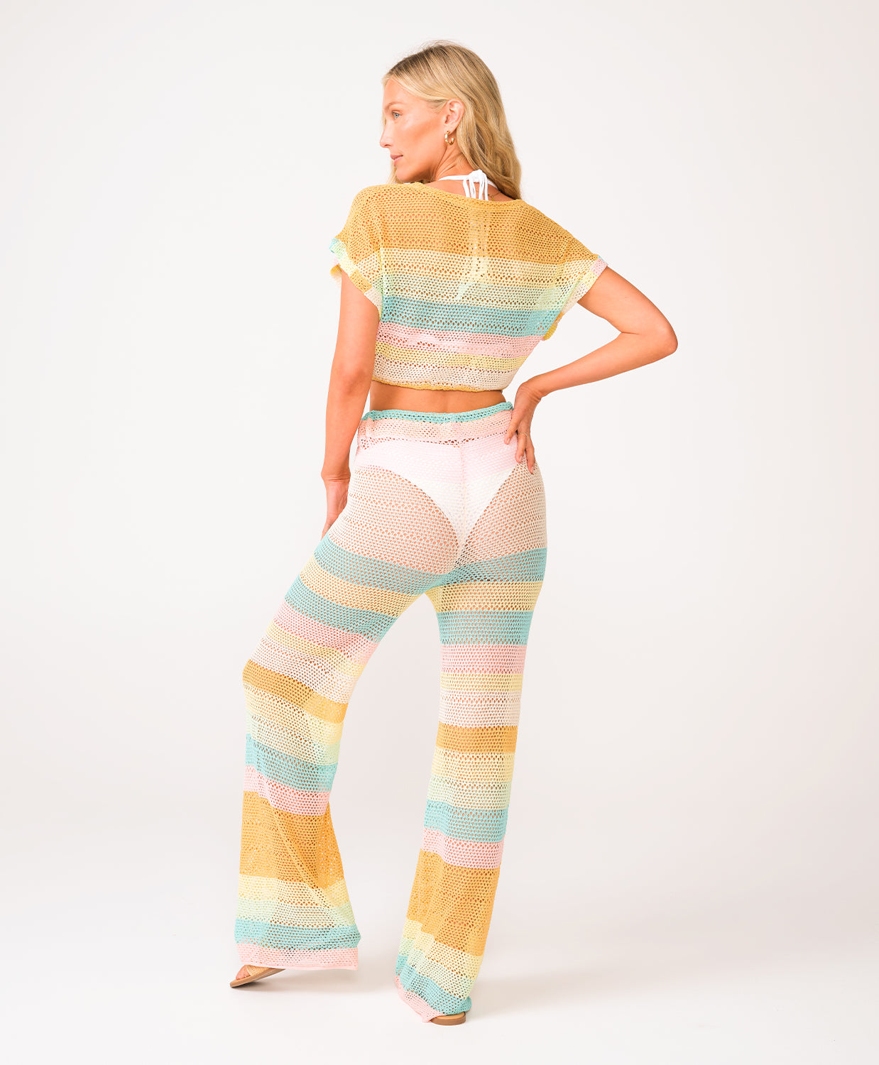 A woman wearing a crochet knit pant and shirt set against a white wall.