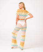 A woman wearing a crochet knit pant and shirt set against a white wall.