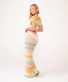 A woman wearing a crochet knit pant and shirt set against a white wall.