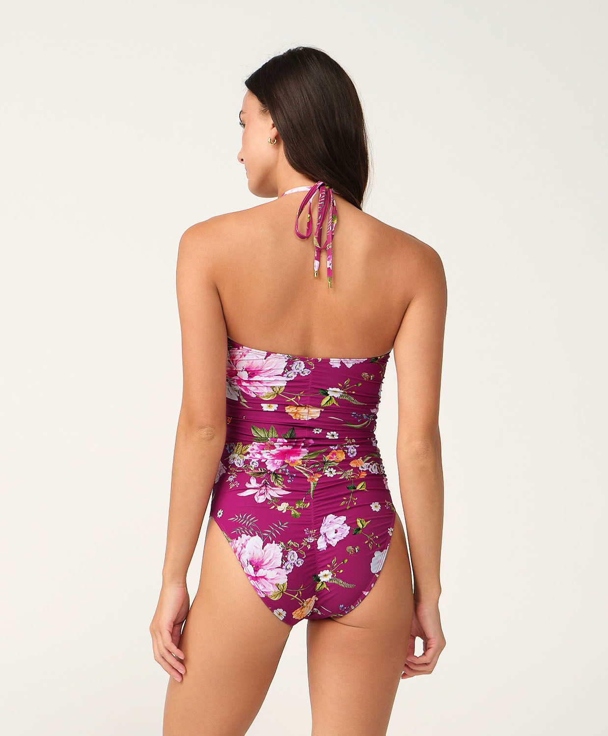 A woman shown from the back wearing a floral one-piece swimsuit with a halter-style neck and tie, against a plain light background.
