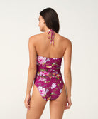 A woman shown from the back wearing a floral one-piece swimsuit with a halter-style neck and tie, against a plain light background.