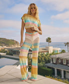 A woman wearing a crochet knit pant and shirt set standing outside near a pool.