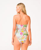 A woman wearing a light blue floral one piece swimsuit facing towards a white wall.
