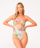A woman wearing a light blue floral one piece swimsuit standing against a white wall.