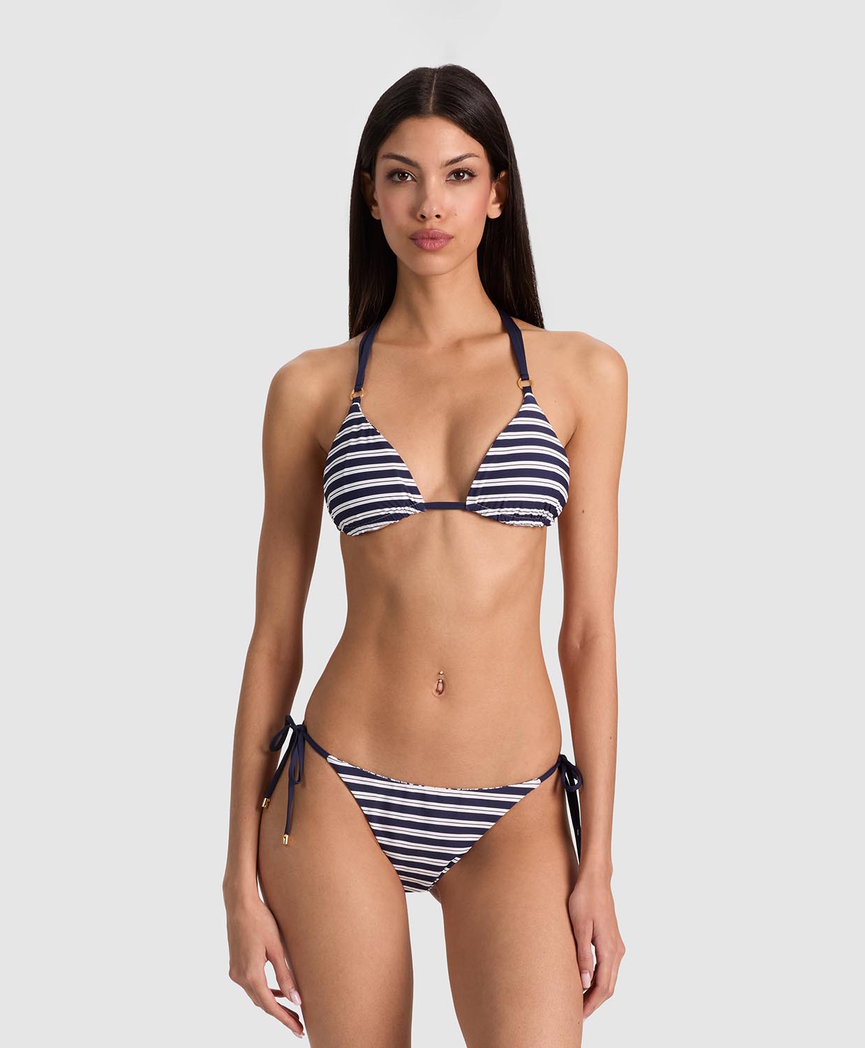 A woman modeling a navy and white striped triangle bikini with side-tie bottoms against a light gray studio background.