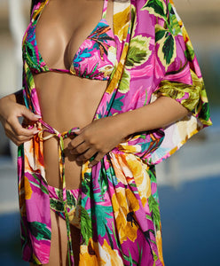 Blonde woman wearing a pink tropical triangle shape bikini with hand-sewn beading and matching coverup standing in front of swimming pool.