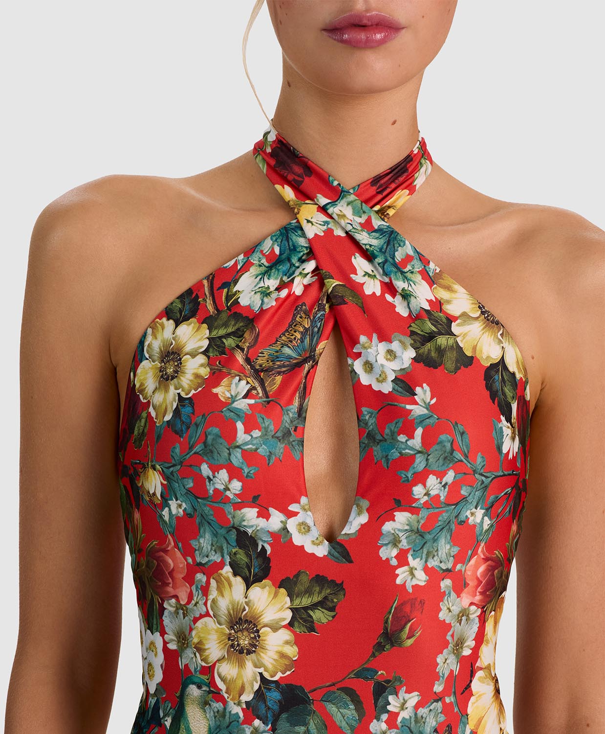 A close-up of a model wearing a red halter-neck dress with a vibrant floral print featuring yellow, white, and green flowers.