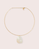 A gold necklace with shell detailing against a white wall.