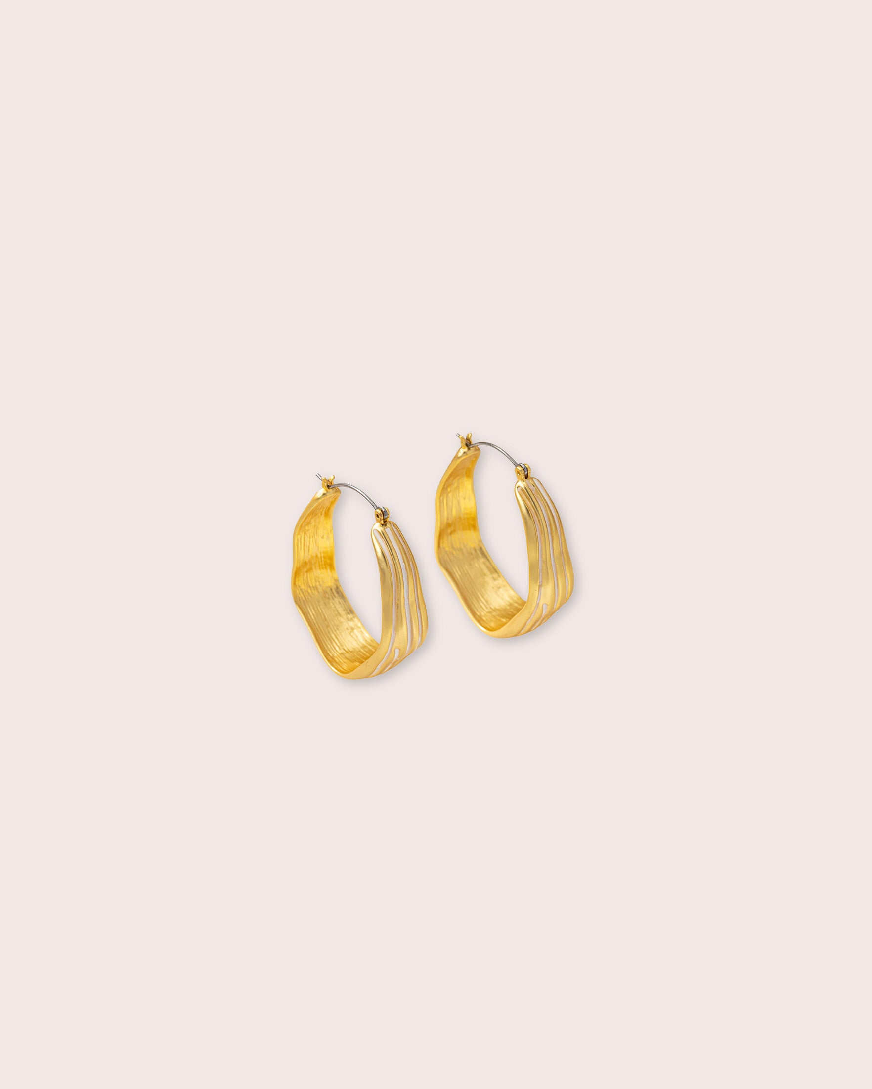 Gold hoop earrings against a white wall.