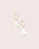 A pair of shell earrings with gold details against a white wall.