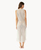 Brunette woman wearing an ivory sleeveless cover up with scalloped lace detailing facing backwards towards white wall.