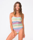 A woman wearing a colorful striped one piece swimsuit standing against a white wall.