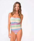 A woman wearing a colorful striped one piece swimsuit standing against a white wall.